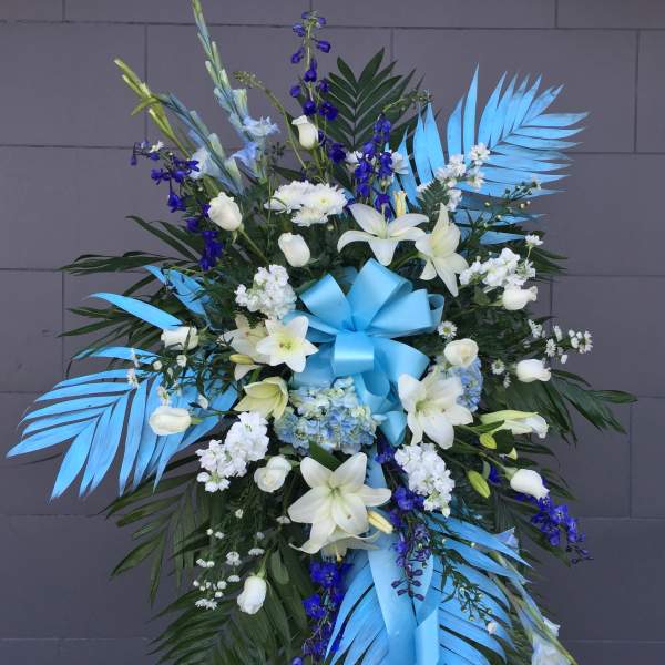 Large blue and white funeral spray with lilies and ribbon on an easel