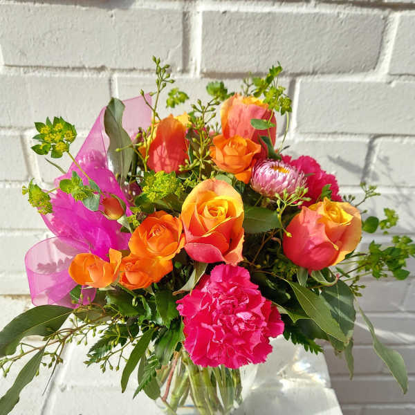 Bouquet of orange and pink roses with carnations in a glass vase