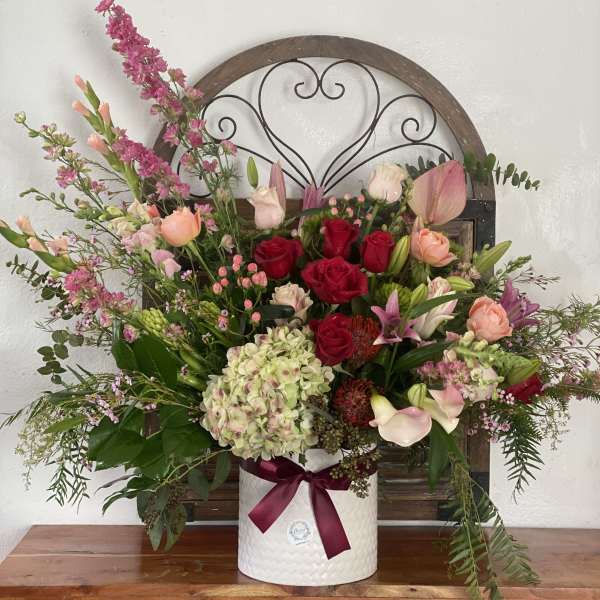Mixed bouquet of roses, lilies, and hydrangea in a white vase with a ribbon