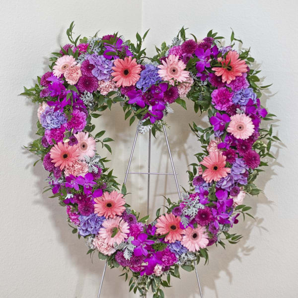 Heart-shaped floral wreath on a metal stand with pink, purple, and lavender blooms