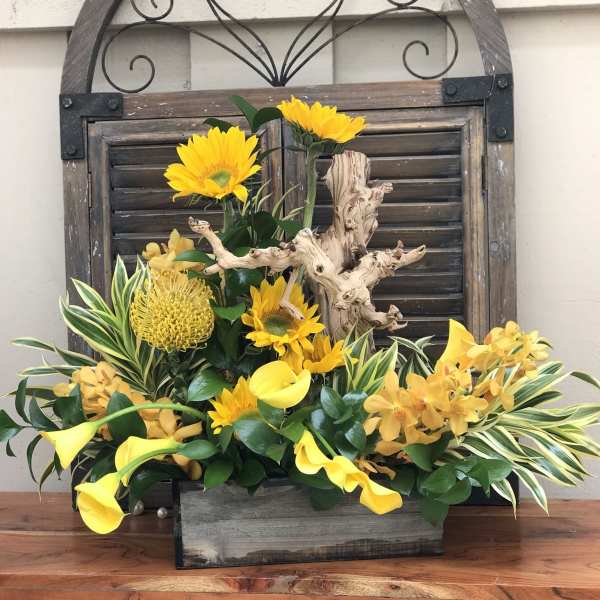 Yellow flowers arranged with calla lilies in a rustic wooden container