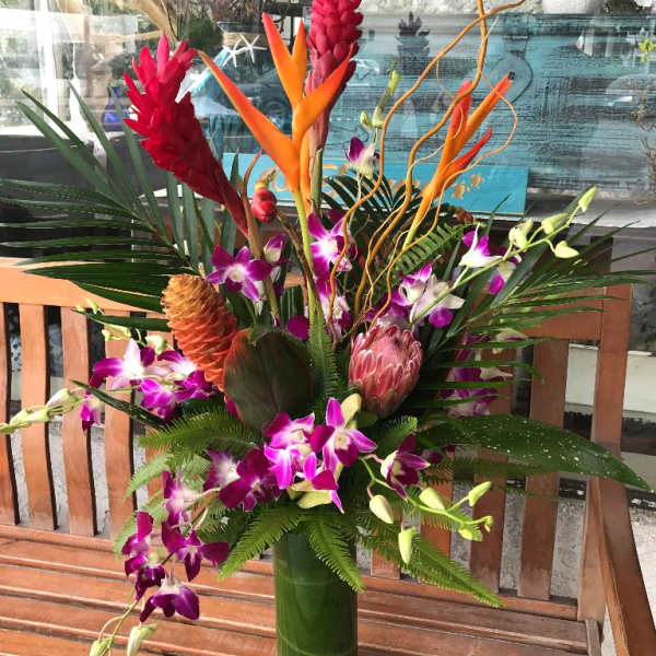 Tropical arrangement with purple orchids, red ginger, and orange heliconia in a tall vase