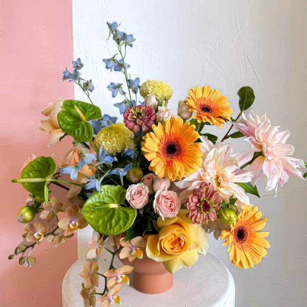 Mixed bouquet in a pink vase with orange, pink, blue, and white flowers