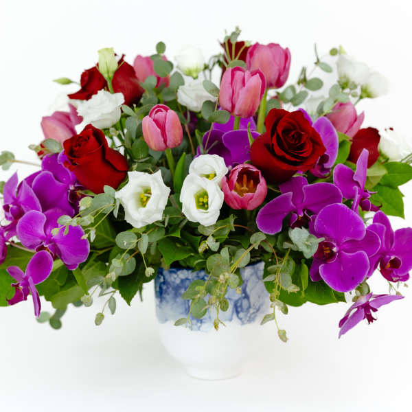 Mixed bouquet of red roses, pink tulips, white blooms, and purple orchids in a vase