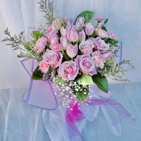 Pink roses and tulips arranged with baby's breath in a wrapped bouquet