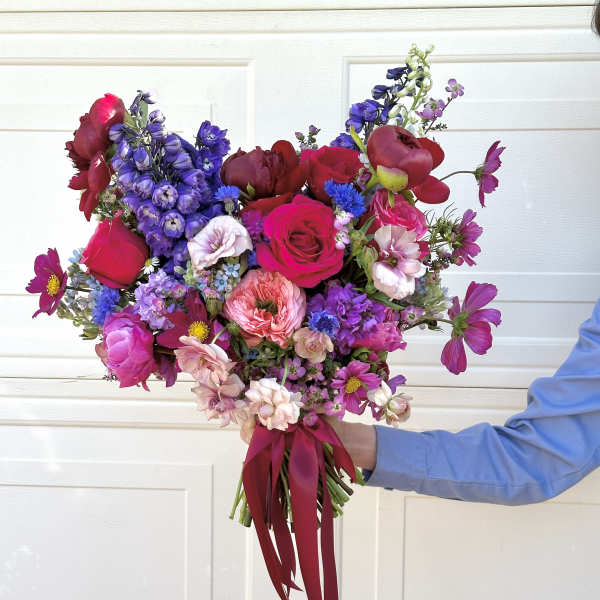 Handheld bouquet of pink, red, and purple flowers tied with a burgundy ribbon.
