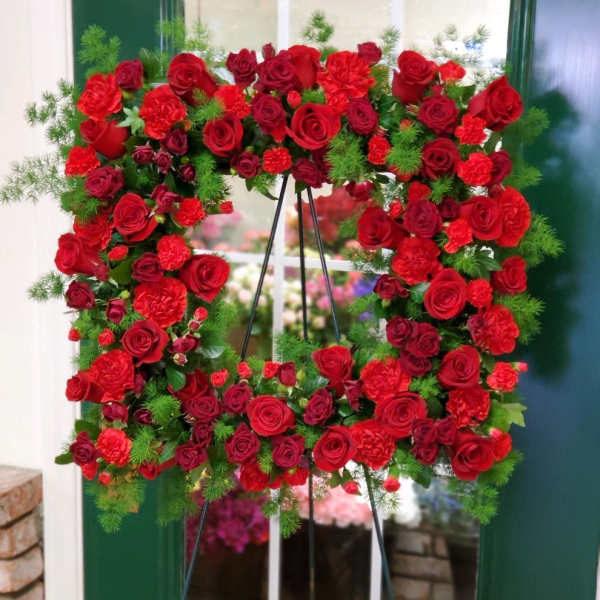 Heart-shaped wreath of red roses and carnations on a stand
