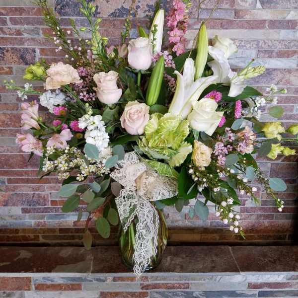 Mixed bouquet of white lilies, pale roses, and pink flowers in a glass vase