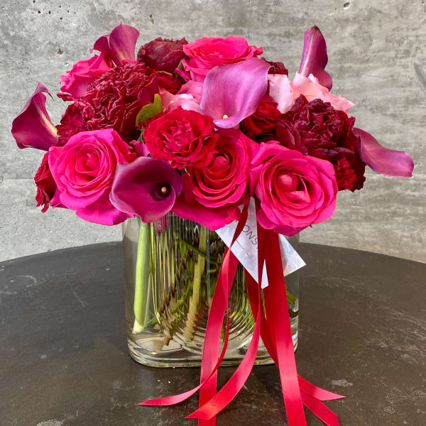 Pink and red roses with purple calla lilies in a clear glass vase