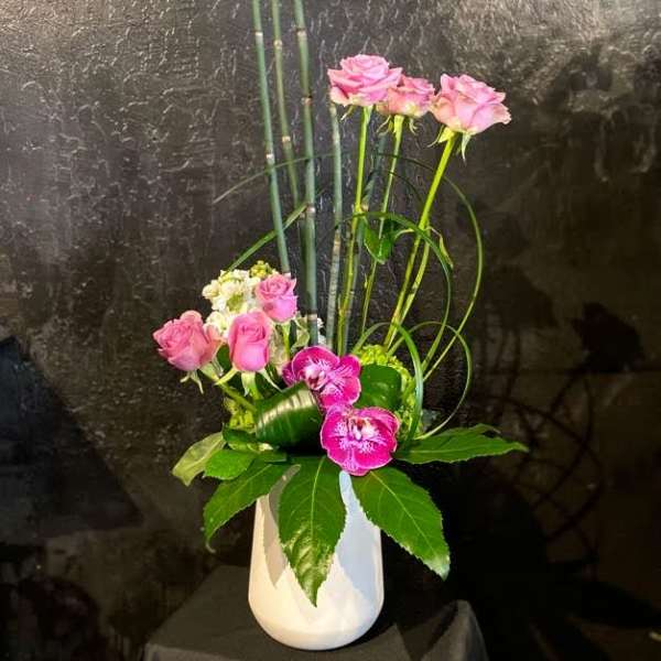 Pink roses and orchids arranged in a white vase with tall bamboo accents.