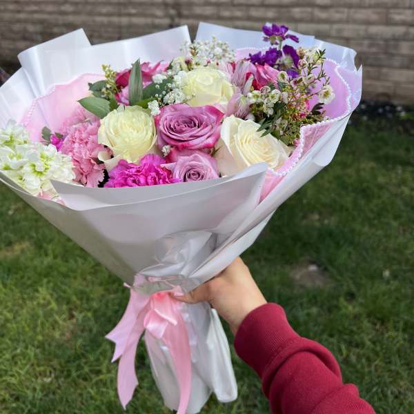 Handheld bouquet of pink and white roses wrapped in white paper