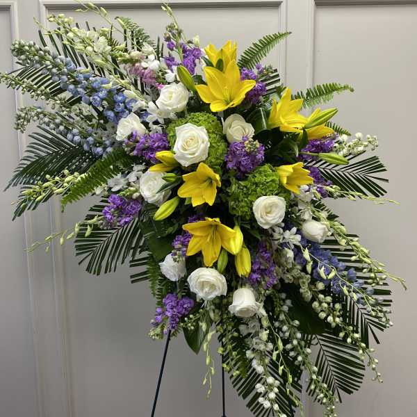 Large standing floral spray with yellow lilies, white roses, and purple flowers
