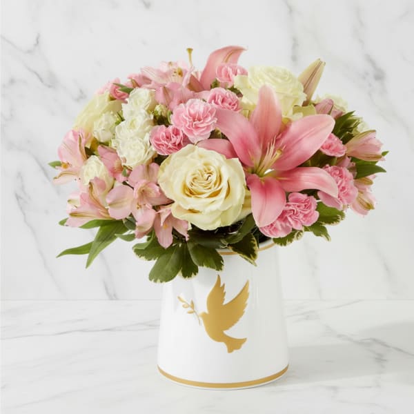 Pink and white flowers arranged in a white vase with a gold dove design.