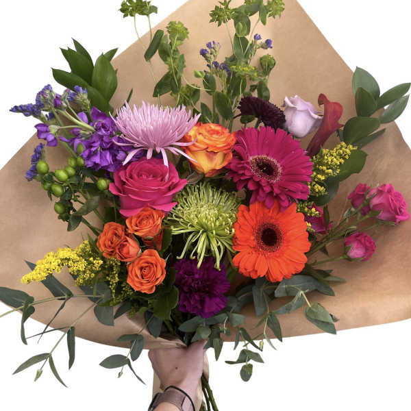Colorful mixed bouquet with roses, gerberas, and purple blooms in brown paper
