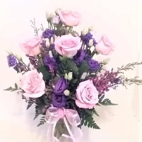 Pink and purple rose bouquet in a clear glass vase with a pink ribbon