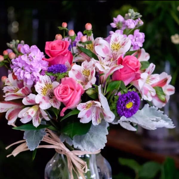 Bouquet of pink roses and purple flowers in a clear glass vase