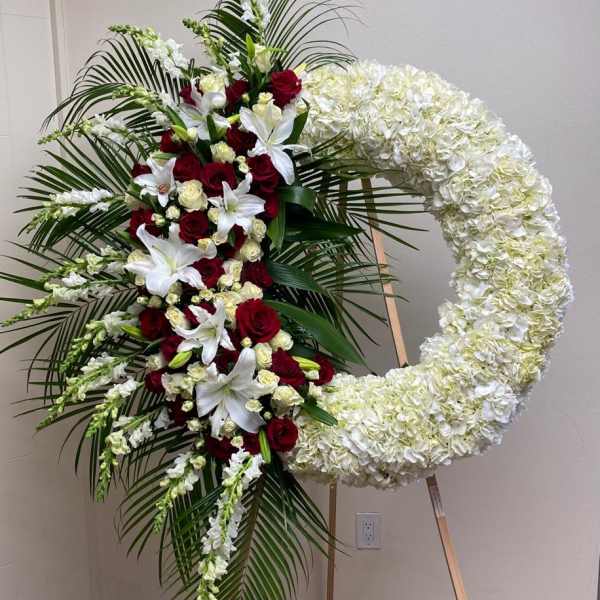 Large floral funeral wreath with red roses, white lilies, and white hydrangeas