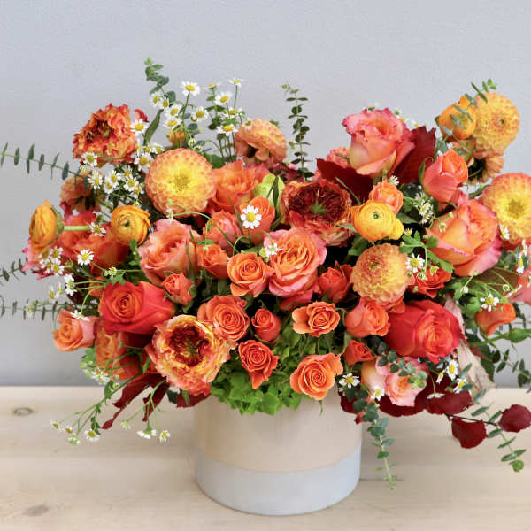 Low arrangement of orange and yellow roses and dahlias in a round white ceramic vase