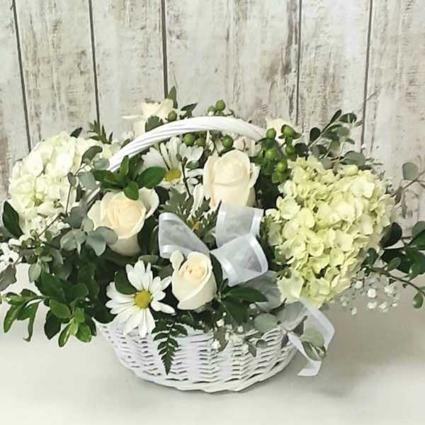 White roses and hydrangeas in a white basket with a ribbon
