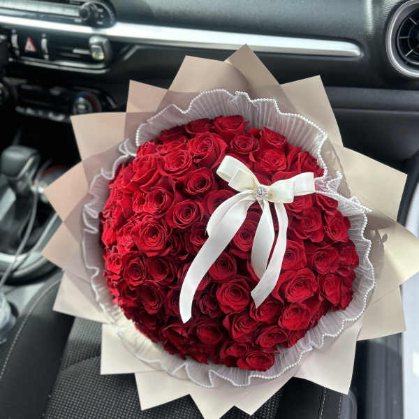 Large bouquet of red roses wrapped in beige paper with a white ribbon
