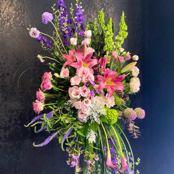 Tall standing spray of pink lilies and mixed purple flowers on a wooden easel.