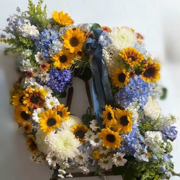 Large floral wreath on an easel with sunflowers, blue hydrangeas, and white blooms