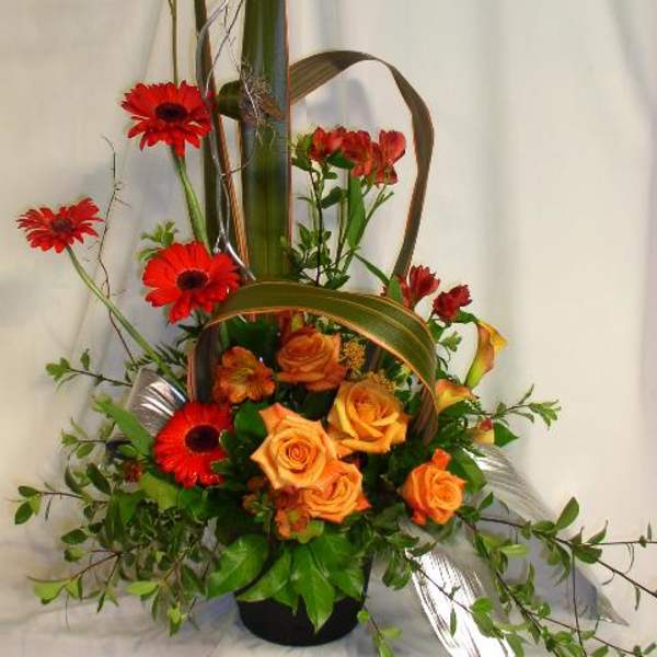 Tall floral arrangement with orange roses and red gerbera daisies in a black vase