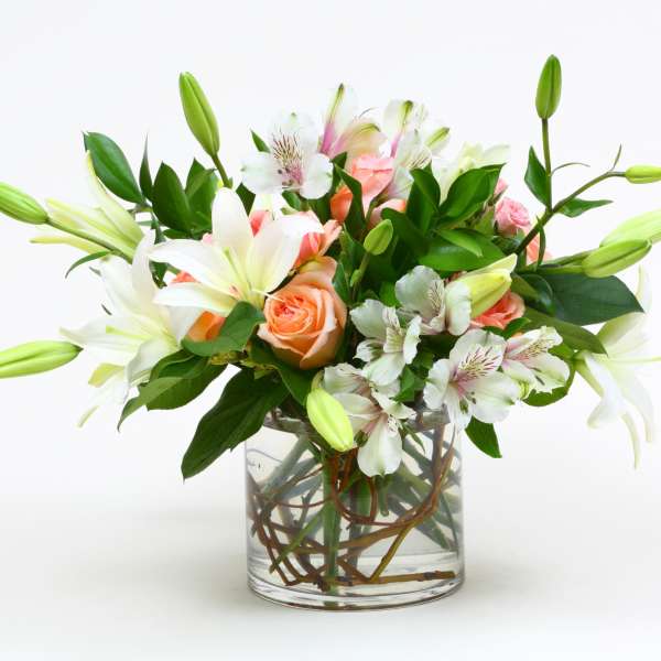 Bouquet of white lilies, peach roses, and white alstroemeria in a glass vase