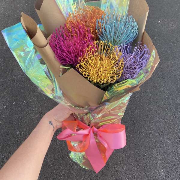 Bouquet of colorful pincushion protea wrapped in brown paper with a pink ribbon