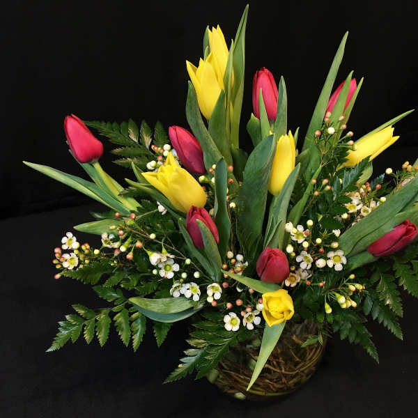Low arrangement of yellow and red tulips with small white blossoms in a clear glass bowl