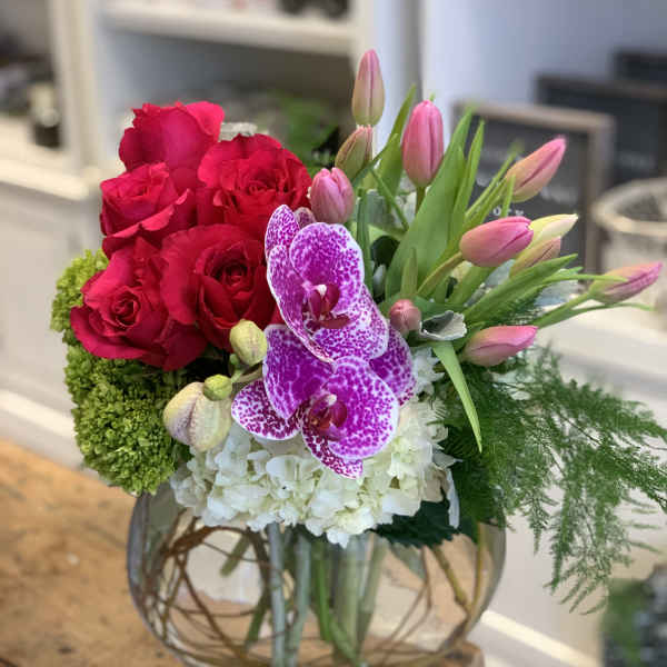 Bright pink roses, tulips and speckled orchids with white blooms in a round glass vase