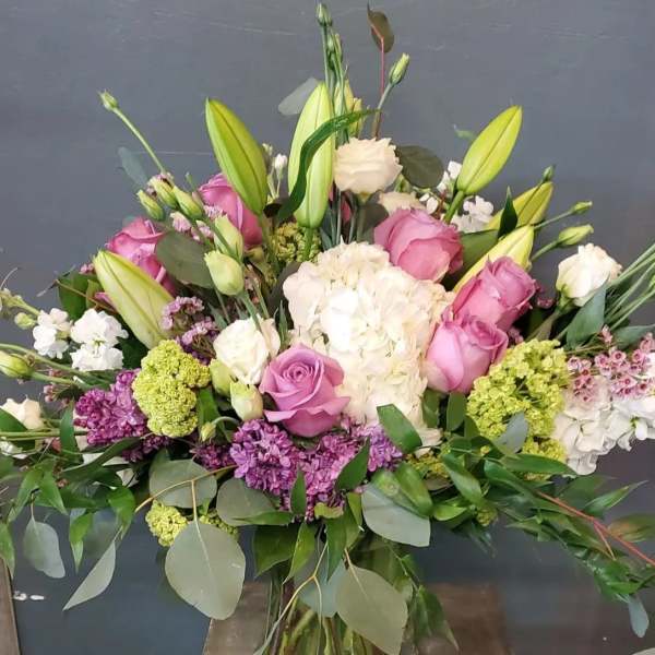 Tall mixed bouquet of pink roses, white hydrangeas, and lilies in a clear glass vase