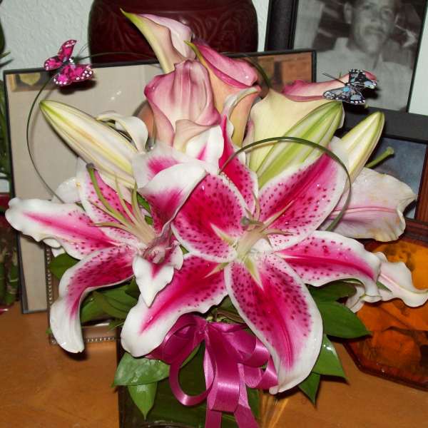 Pink and white lilies arranged in a glass vase with a ribbon and butterfly picks.