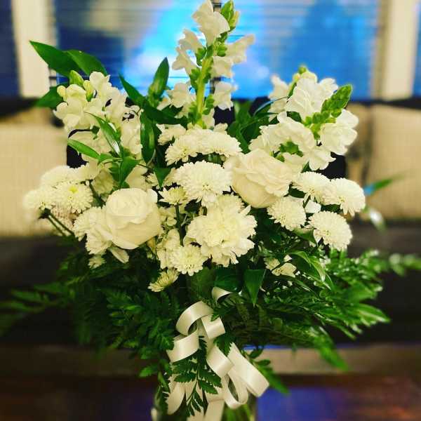 White flowers arranged in a tall glass vase with a ribbon bow