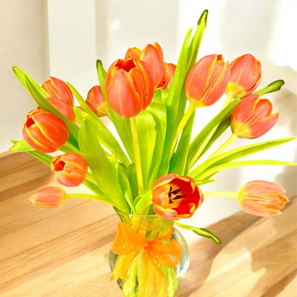 Orange tulips in a glass vase with an orange ribbon