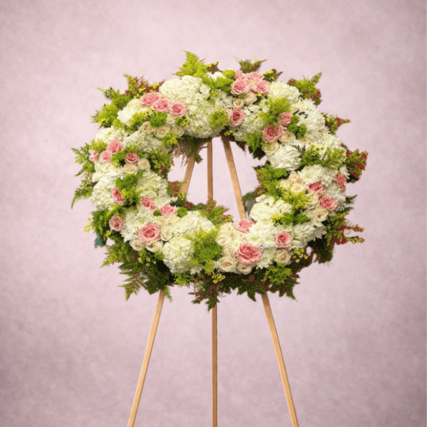 Standing wreath of white and pink flowers with green accents on a wooden easel.