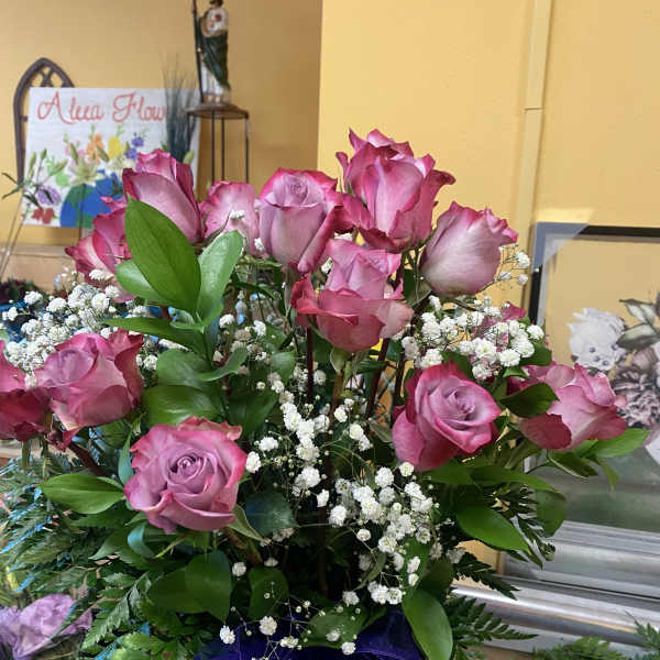 Pink roses arranged in a glass vase with white baby's breath and purple ribbon