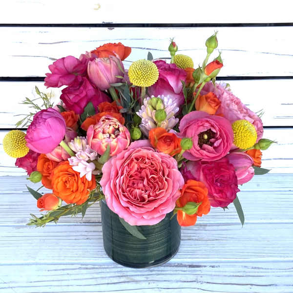 Bright arrangement of pink and orange roses, ranunculus, and tulips in a green glass vase