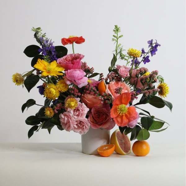 Mixed bouquet in a white vase with oranges and grapefruit at the base