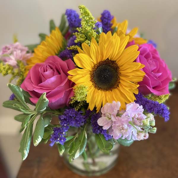 Bouquet of sunflowers, pink roses, and purple filler flowers in a glass vase