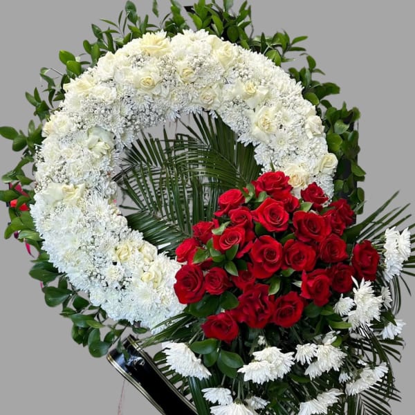 White floral wreath with red roses and greenery on a stand