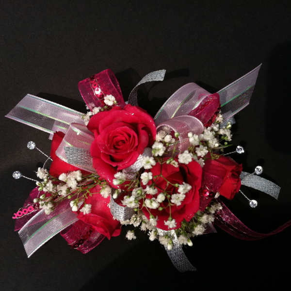 Red rose corsage with baby's breath and silver ribbon on a black background