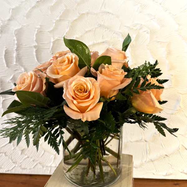 Peach roses arranged in a clear glass vase with greenery