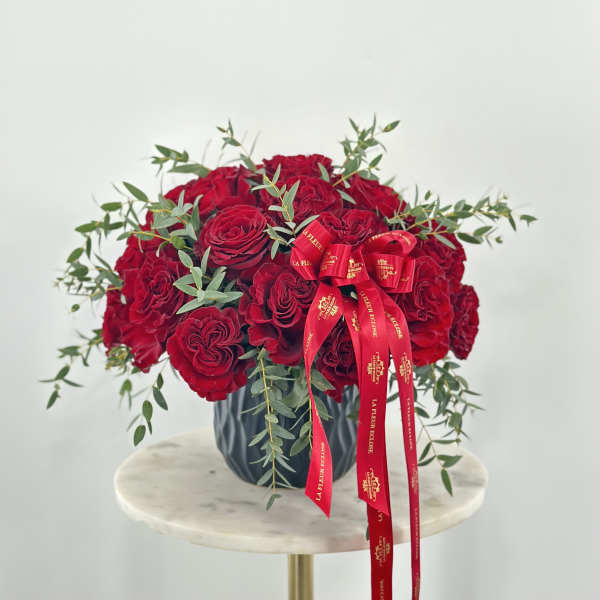Red rose arrangement in a dark vase with a red ribbon