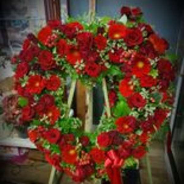 Heart-shaped standing wreath of red flowers with a red ribbon bow on an easel