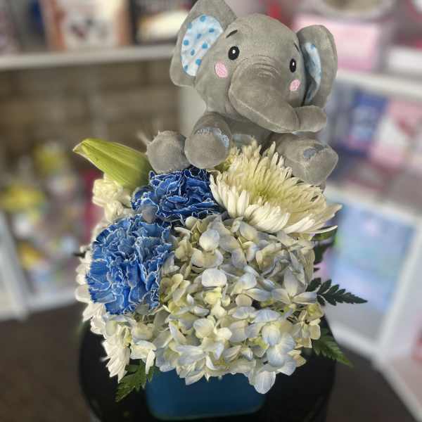 Plush elephant sitting on a blue floral arrangement