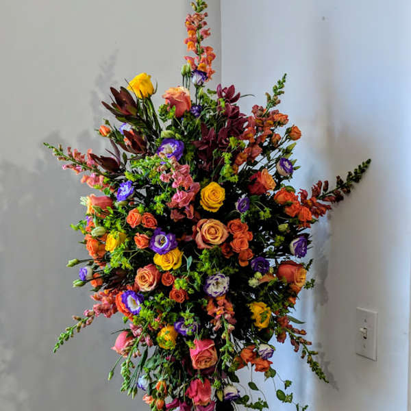 Tall multicolor standing spray with roses, lisianthus, and snapdragons on a black stand