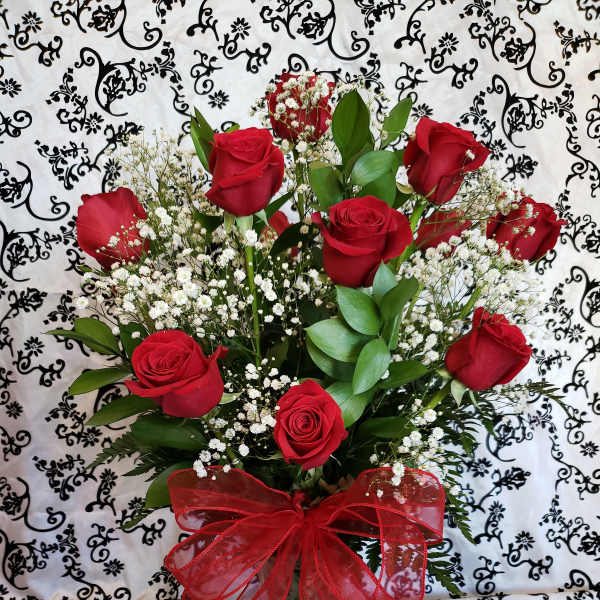 Red roses in a glass vase with baby's breath and a red bow