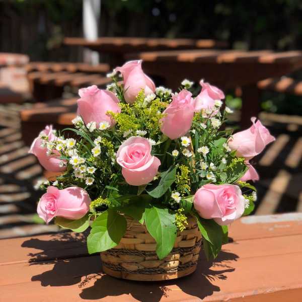 Pink roses arranged in a woven basket with small white filler flowers