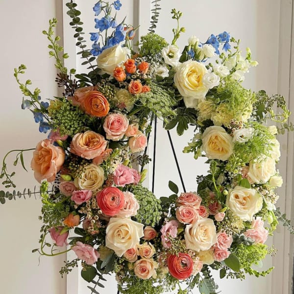 Large floral wreath with roses, ranunculus, and blue delphinium on a stand